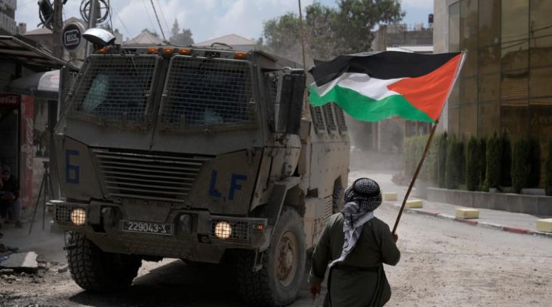 Seorang pria mengibarkan bendera Palestina saat kendaraan lapis baja Israel bergerak selama operasi militer di kamp Nur Shams, di Tepi Barat, Kamis, 29 Agustus 2024.