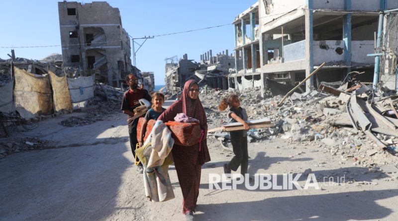 Warga Palestina, Amal Alyan bersama keluarganya berjalan di lingkungan rumah mereka yang hancur akibat serangan Israel, di Kota Gaza, Ahad (26/10/2025).